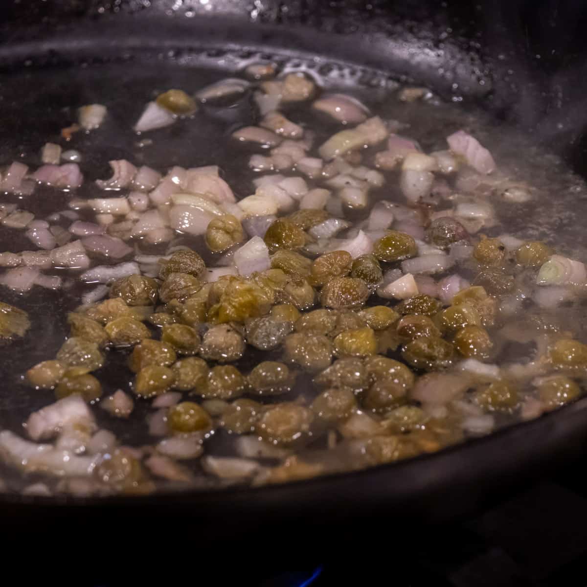 Shallots and capers in a skillet.