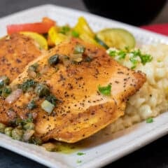 A wide image of a plate with fish, risotto and sautéed vegetables.