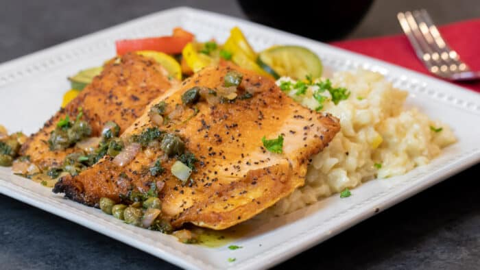 A wide image of a plate with fish, risotto and sautéed vegetables.