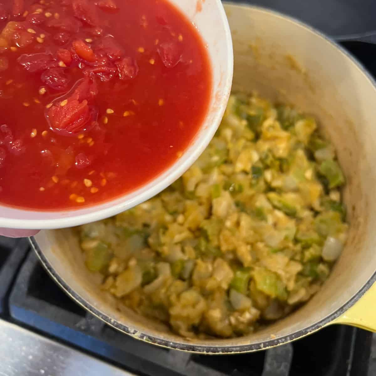 Tomatoes in a bowl being poured into dutch oven.