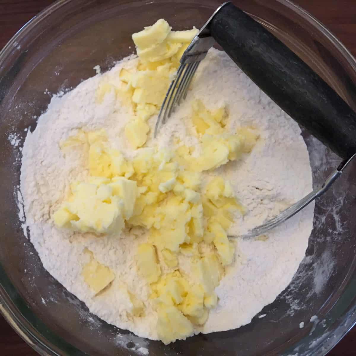 A glass mixing bowl with flour and cold butter.