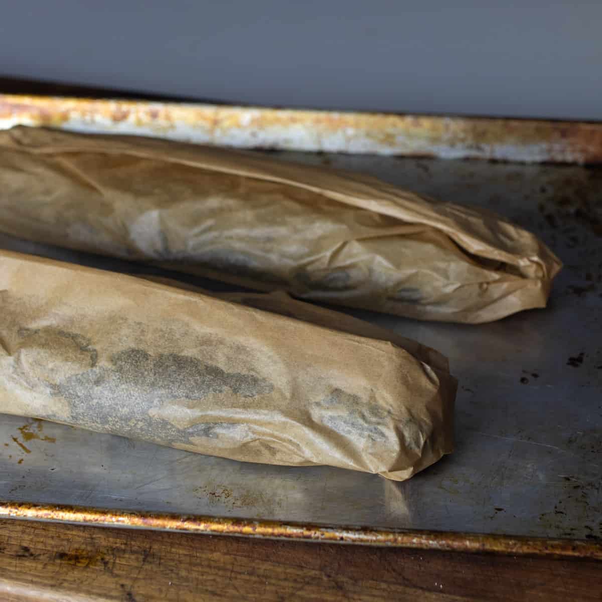 Two fish wrapped in paper and lying on a baking sheet.