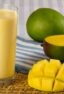 A glass of mango drink next to two mangos.