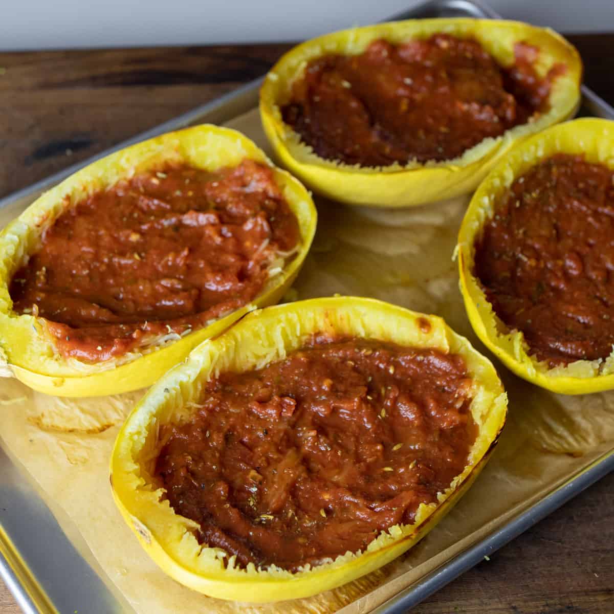 Baked squash halves with pizza sauce spread in the hollowed out area.