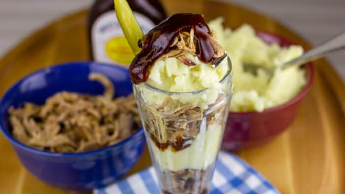 Pulled pork parfait in front of bowls of pork and mashed potatoes.