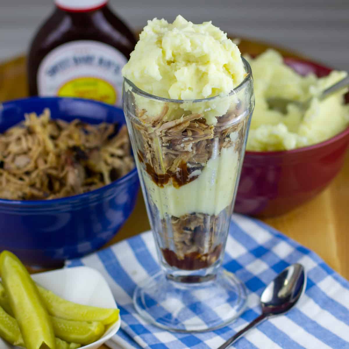 Layers of pulled pork and mashed potatoes added to a tall bowl.