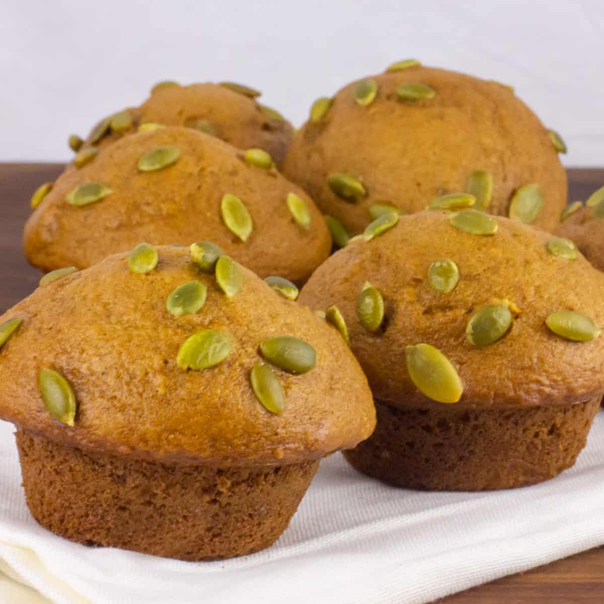 Five muffins that are topped with pepitas.
