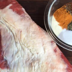 A bowl of spices next to a large beef roast.