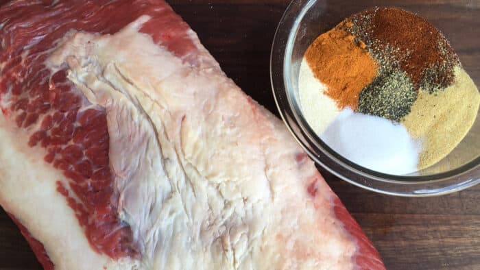 A bowl of spices next to a large beef roast.