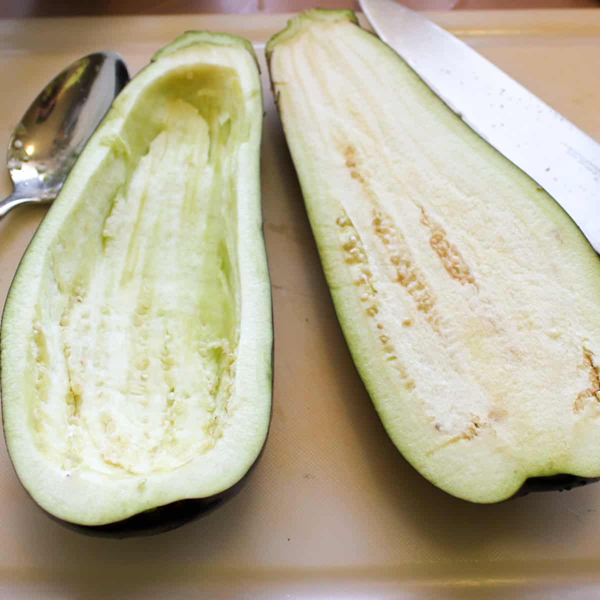 An eggplant on a cutting board cut in half with the insides scooped out.