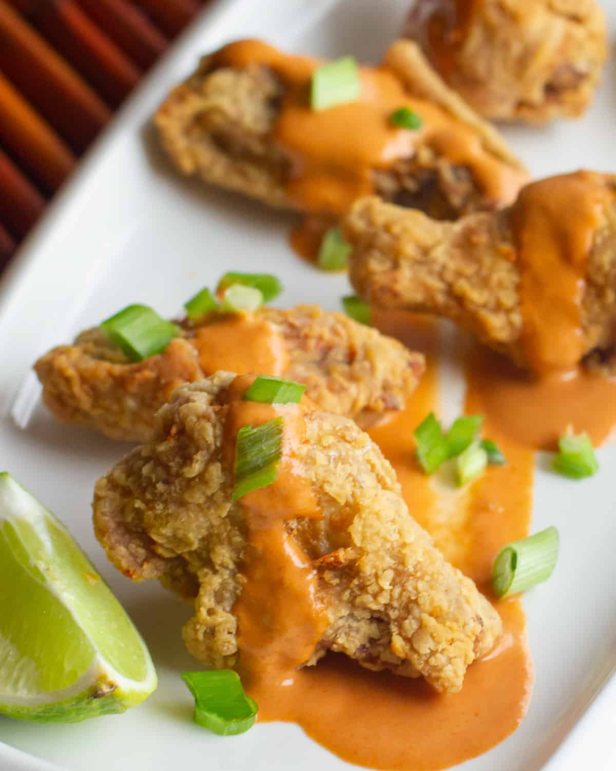 A plate with wings, sauce and sliced green onions.