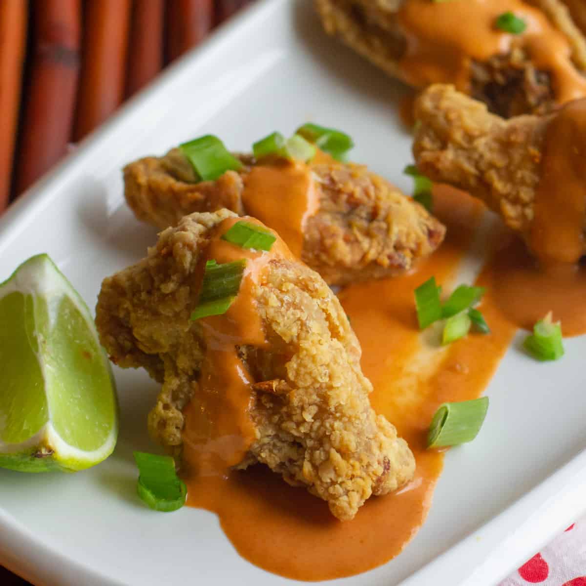 Close up picture of fried wings on a plate with lots of sauce.