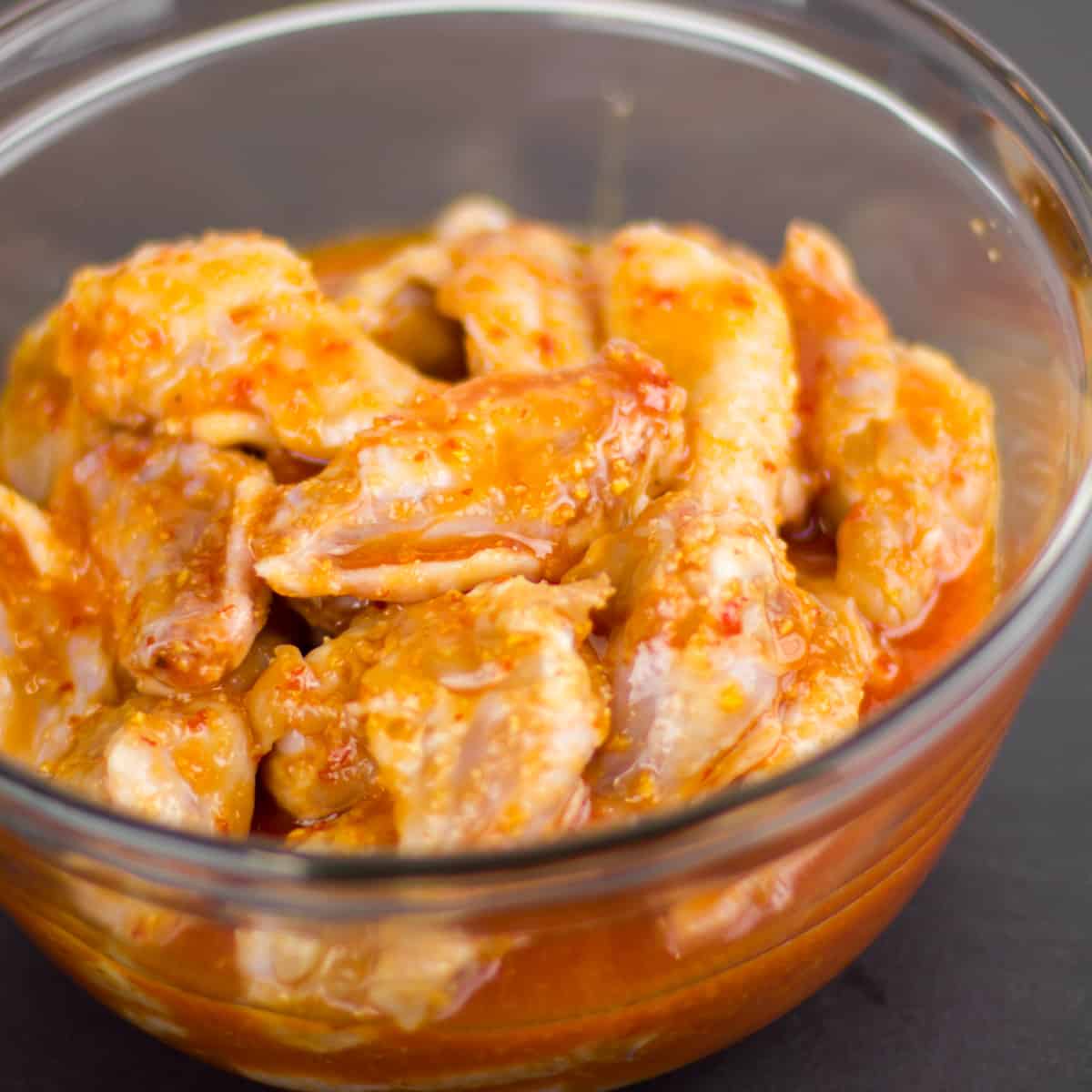 Chicken wings marinating in a glass mixing bowl.