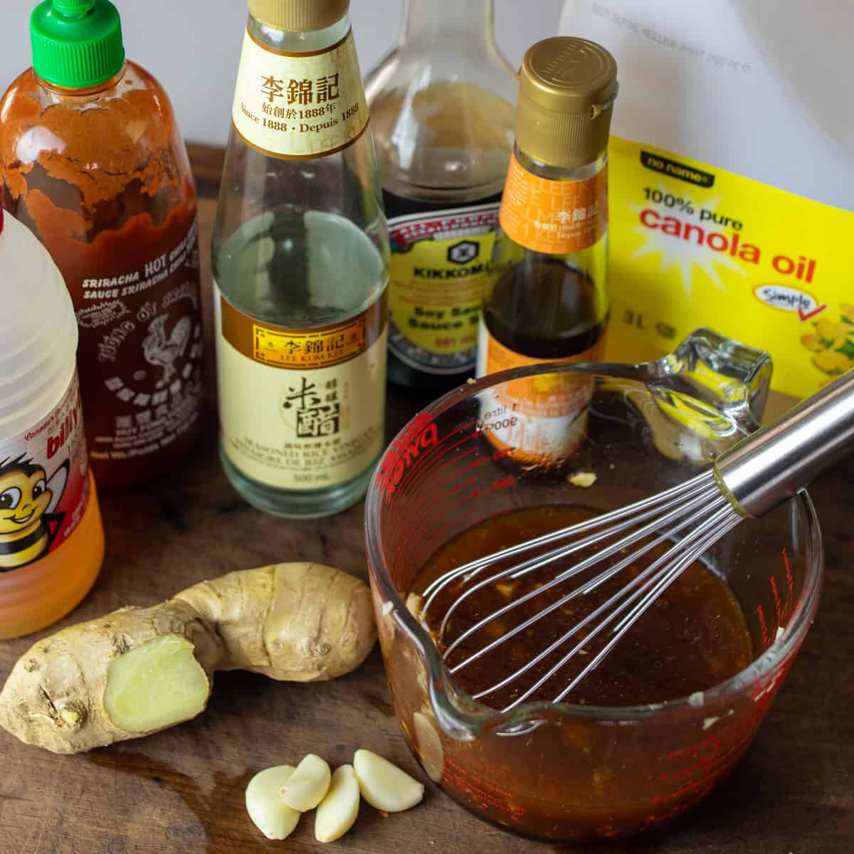 Salad dressing mixed in a measuring bowl with ingredient bottles surrounding.