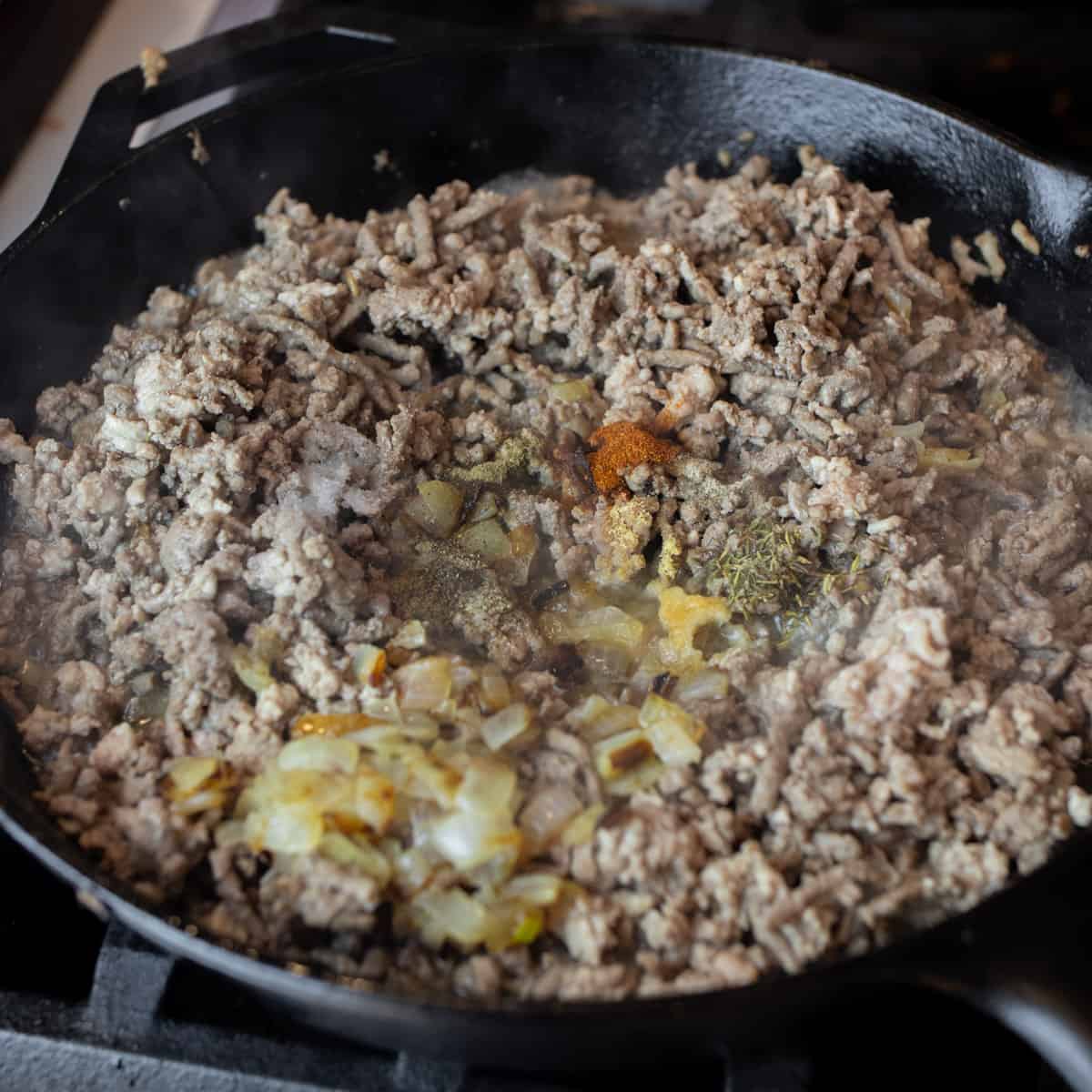 Cooked ground beef and pork in a skillet with onions and seasoning.