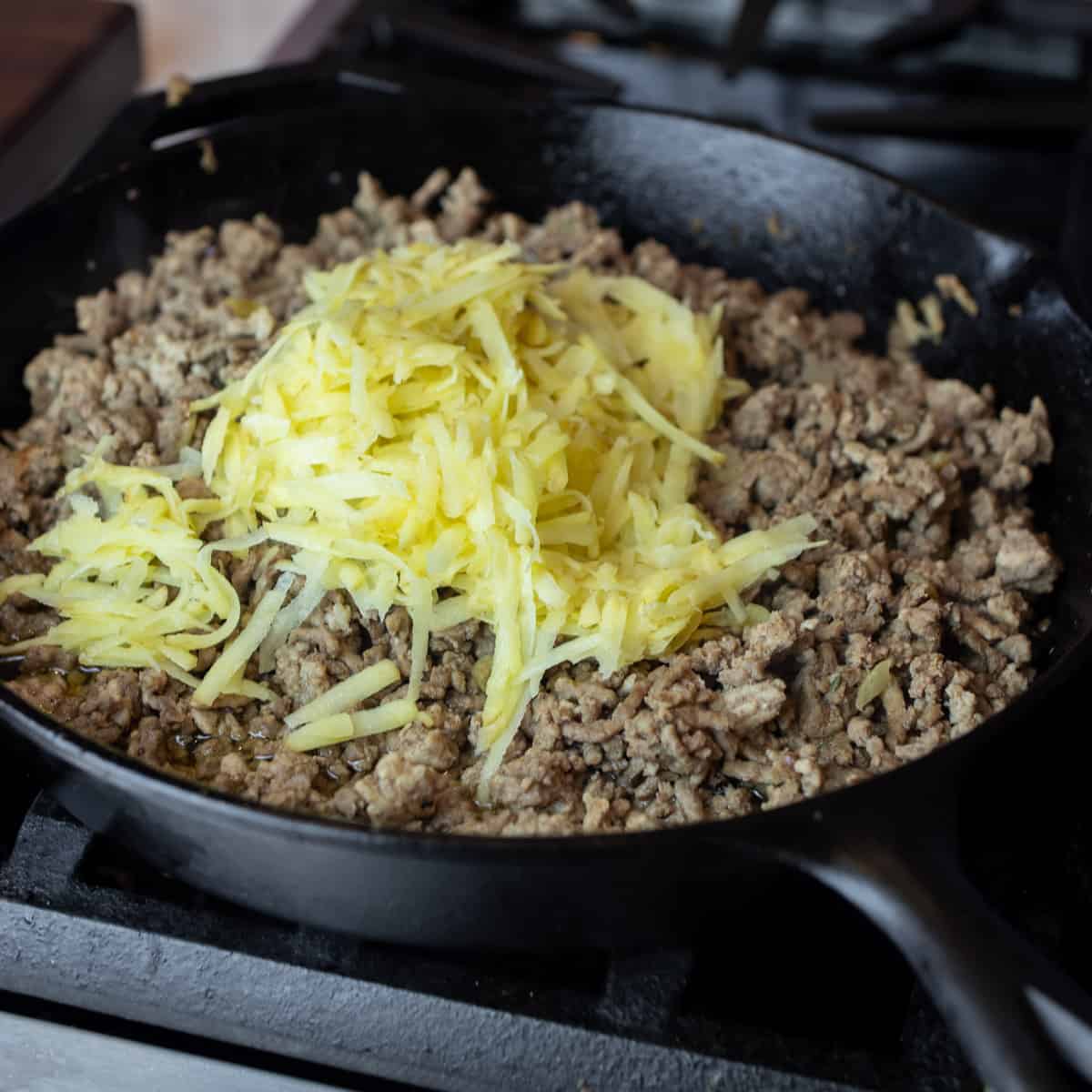 Grated raw potatoes added to a pan with ground beef.