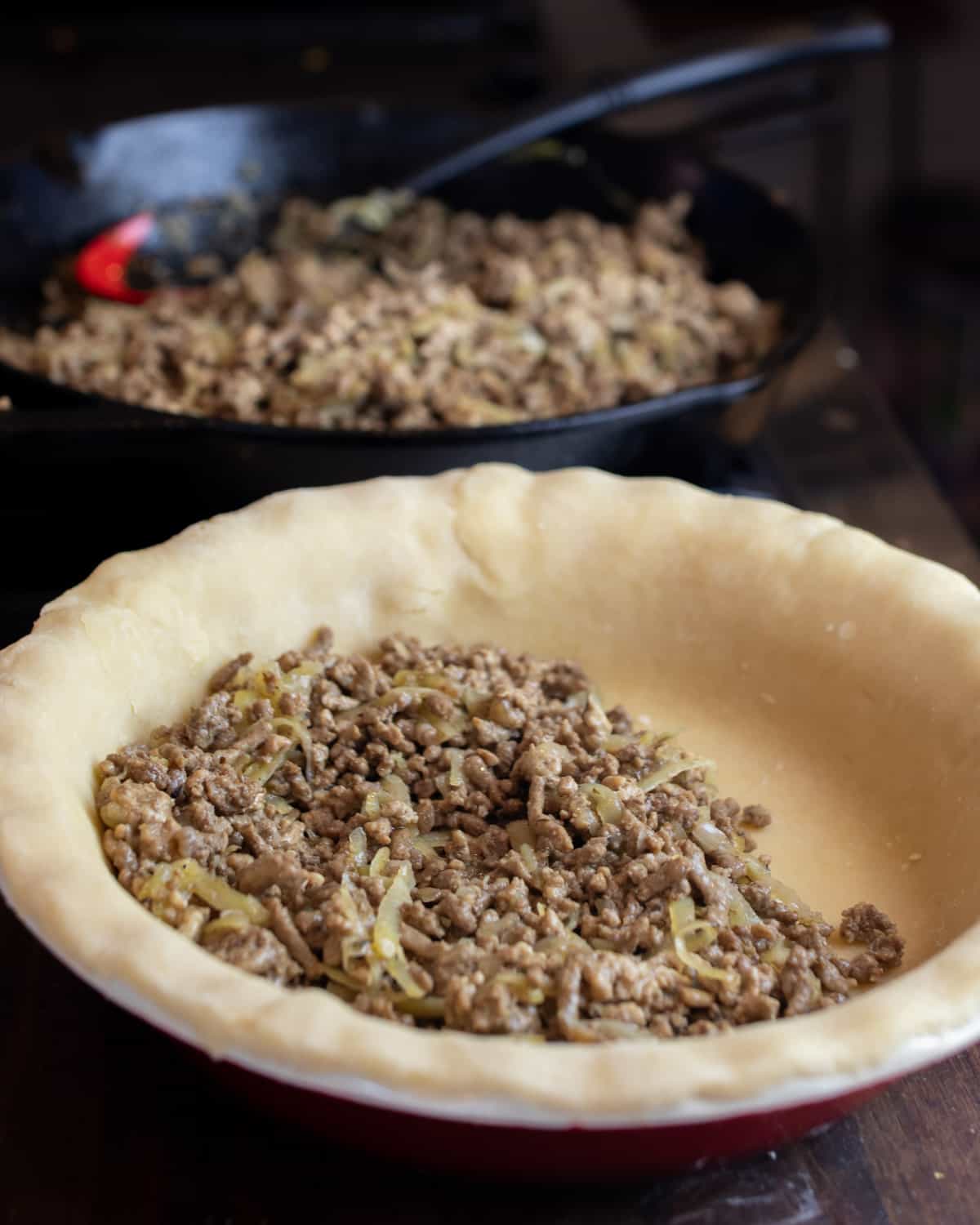 Meat filling being added to a raw pie shell.