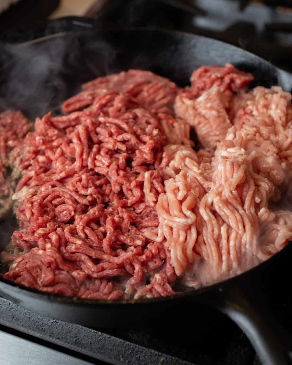 Raw ground beef and ground pork cooking in a skillet.