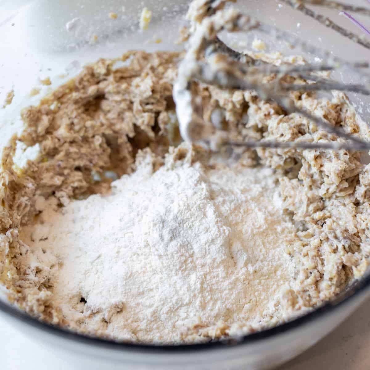 A mixing bowl with cookie dough and a pile of flour just added on top.