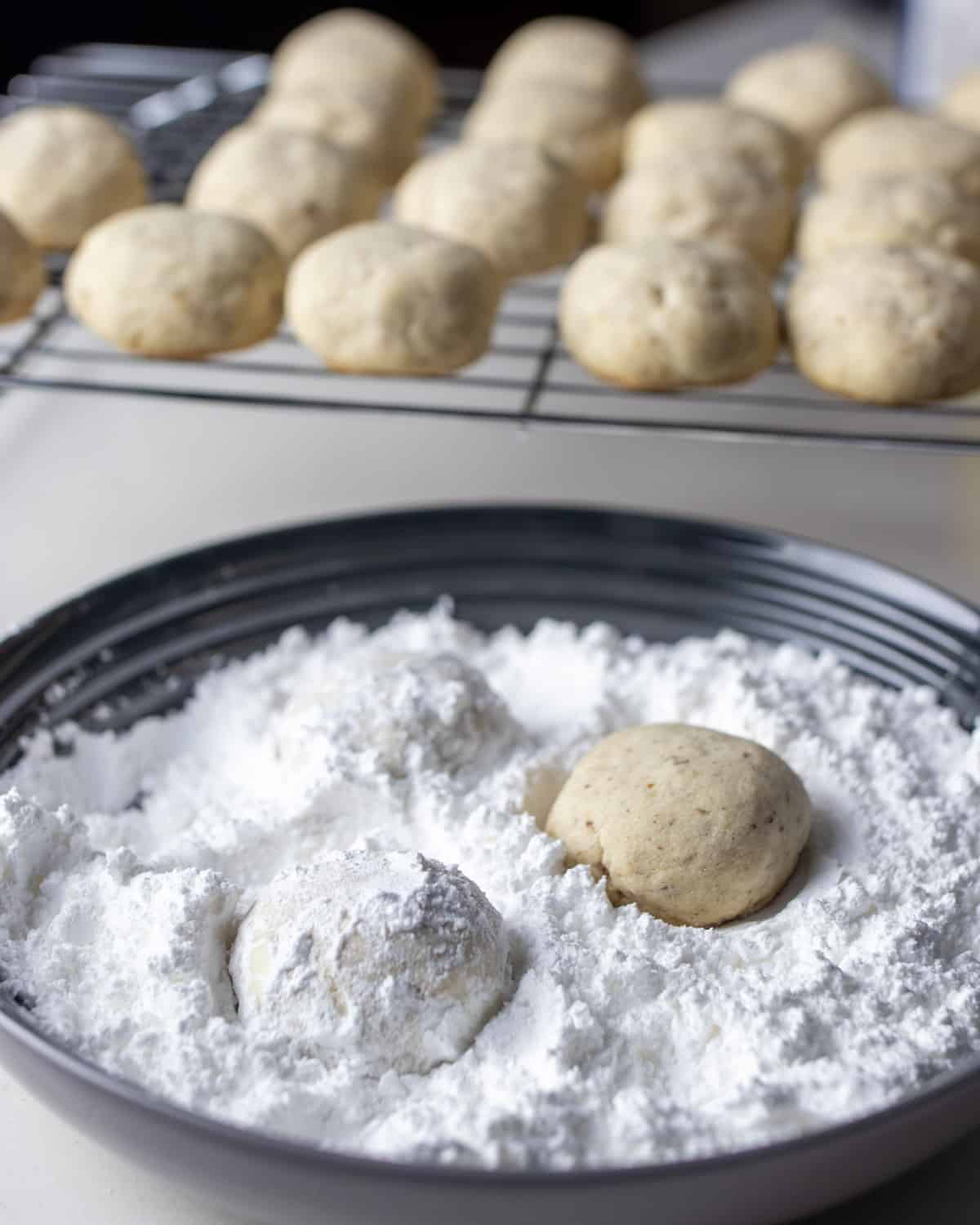 Baked cookies in a bowl of icing sugar.