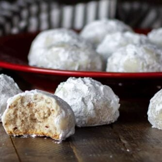 Round shaped cookies dusted in icing sugar with some on a plate and one having a bite out of it.