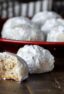 Round shaped cookies dusted in icing sugar with some on a plate and one having a bite out of it.