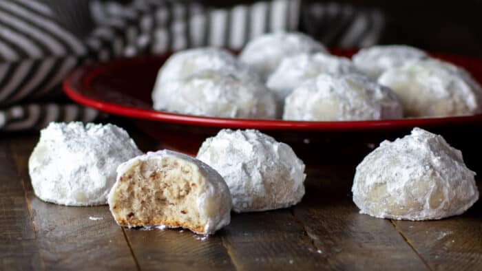 Round shaped cookies dusted in icing sugar with some on a plate and one having a bite out of it.