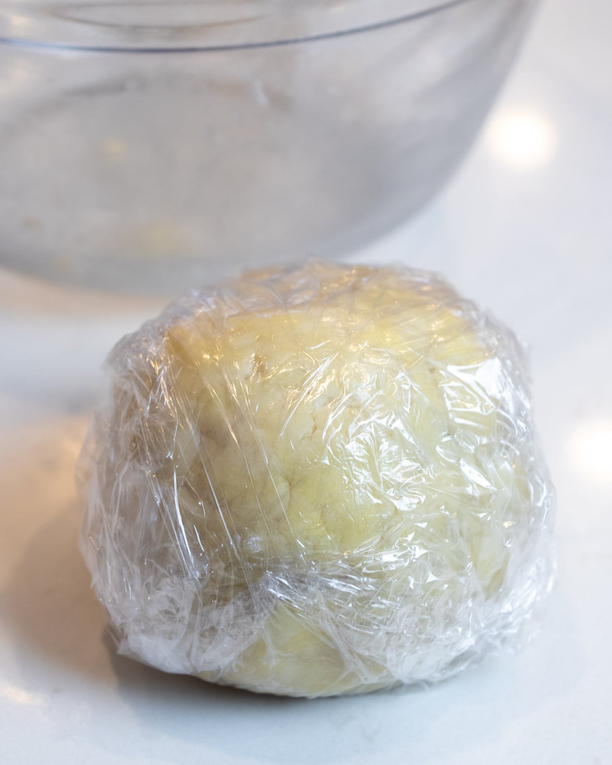 Ball of pie dough wrapped in plastic wrap.