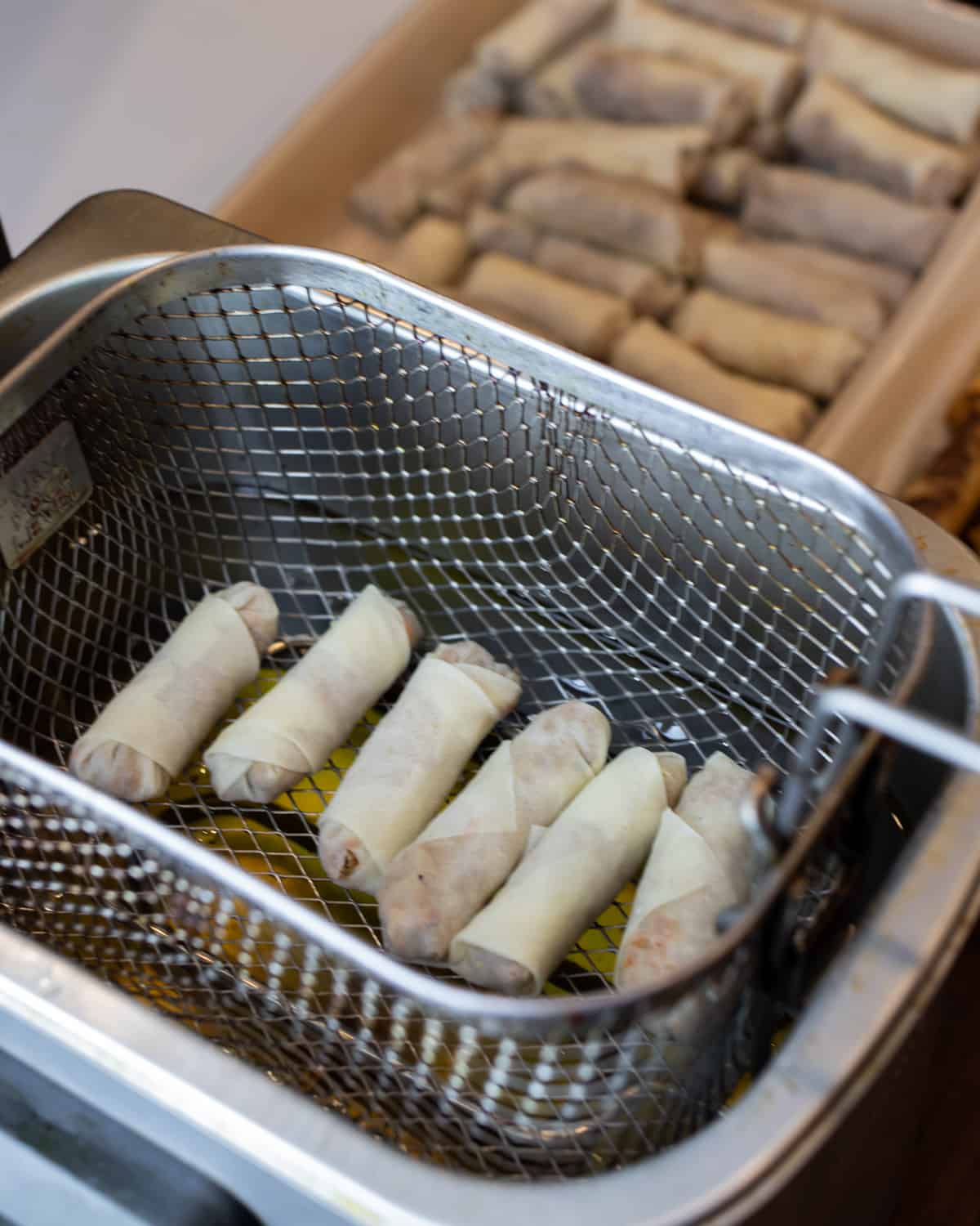 Six spring rolls in a deep fryer basket.