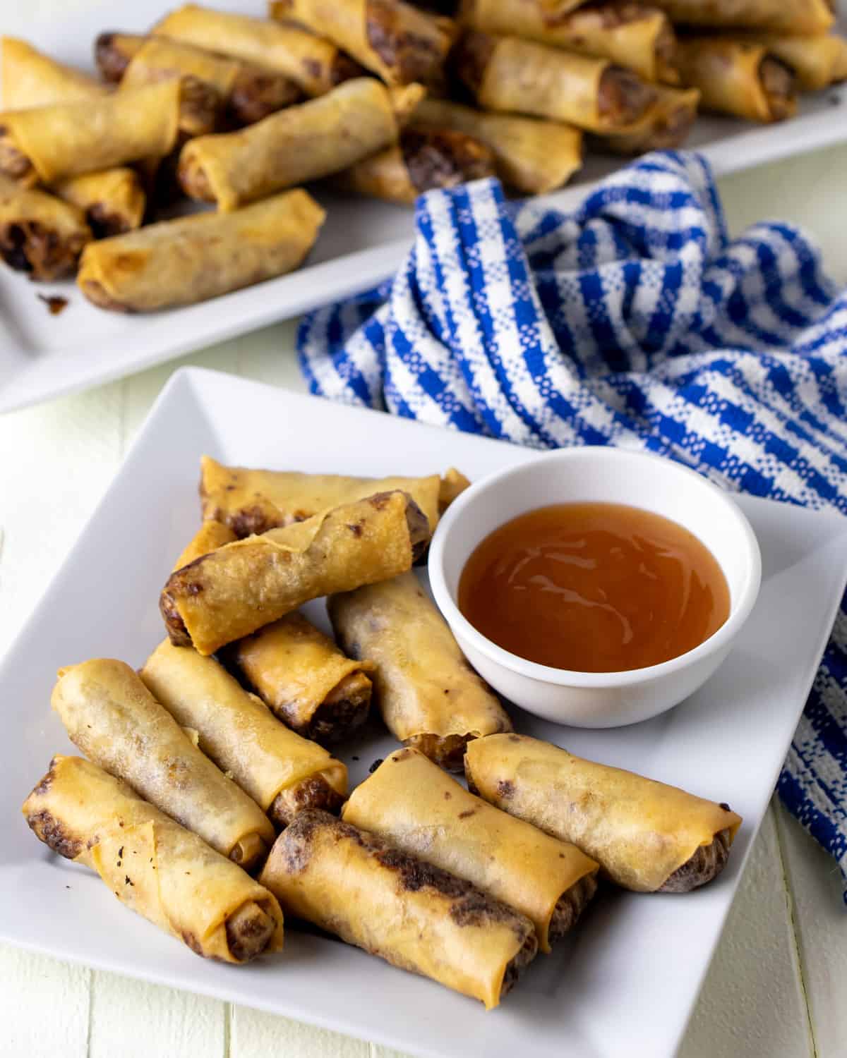 Pork spring roll lumpia on a plate with a small bowl of plum sauce. 