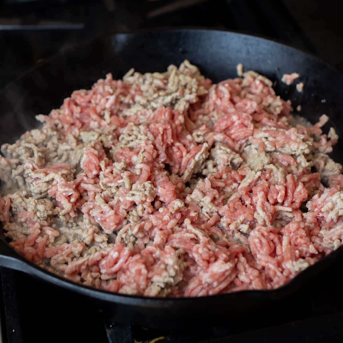 Ground pork in a cast iron skillet being cooked.