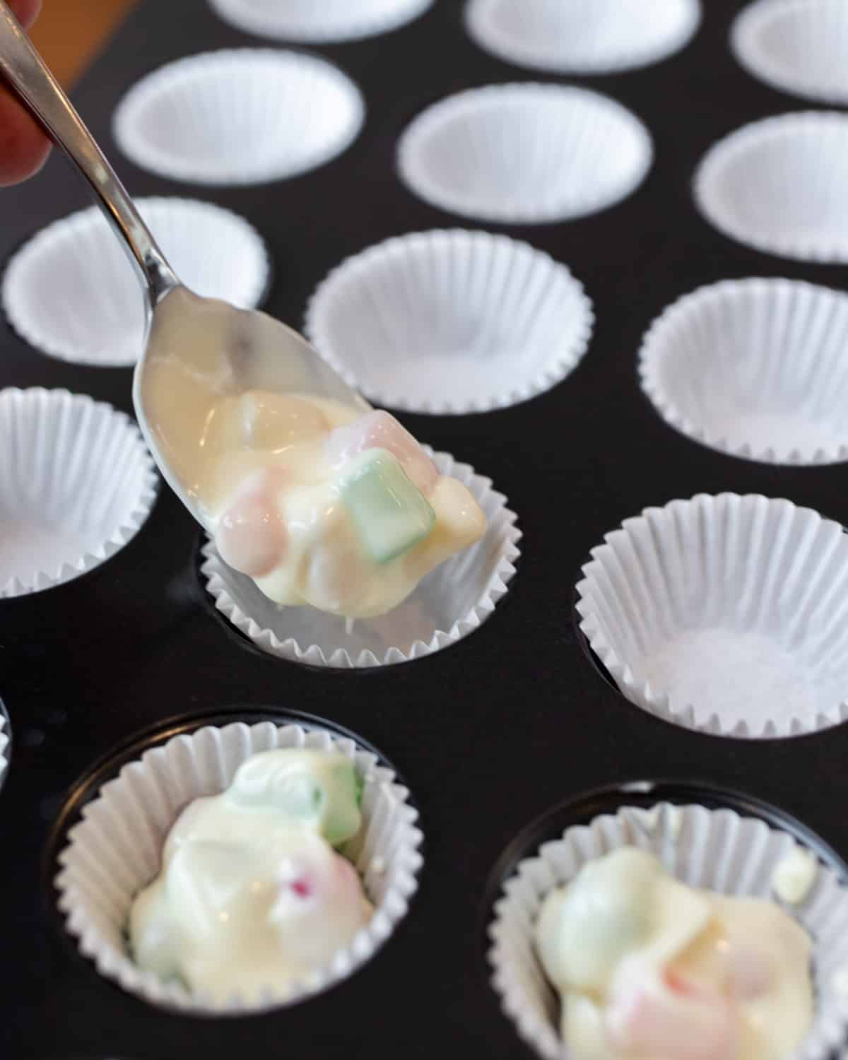 melted chocolate being spooned into paper liner cups.