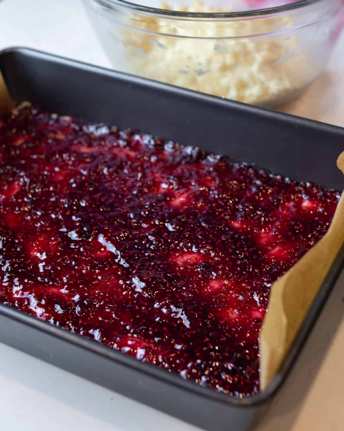 Raspberry jam spread on a cookie mixture in a baking pan.